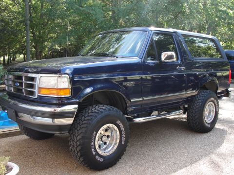 1967 Ford Mustang - This dark blue Ford Bronco is shown from a three-quarter front angle, highlighting its off-road modifications.