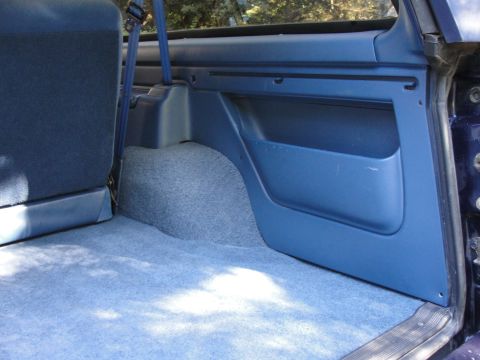 1967 Ford Mustang - Interior view of a blue carpeted cargo area with a plastic door panel and seatbelt visible.