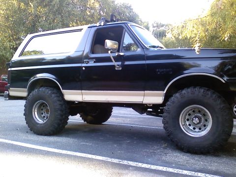 1990 Ford Bronco - Side view of a modified 1990 Ford Bronco with lifted suspension and oversized tires.