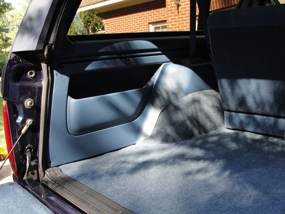 Rear interior of a dark blue Ford Bronco, showing carpeted floor and blue plastic trim panels