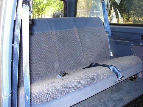 1967 Ford Mustang - The interior of a vehicle shows a blue fabric rear bench seat with seatbelts. A watermark is visible in the lower right corner.