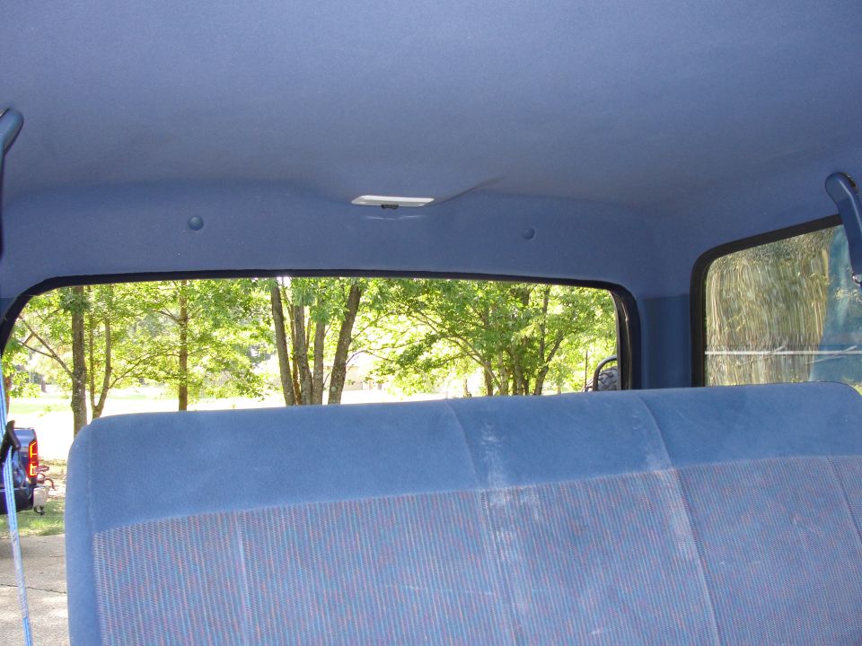 Blue fabric seat and headliner inside a vehicle, with trees visible through the rear window