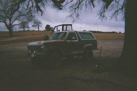 1986 Ford Bronco - A Ford Bronco sits in a muddy field under a cloudy sky, with a shovel nearby.