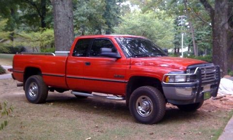 1989 Ford Bronco - This red pickup truck is parked outdoors on a grassy area with trees and foliage visible.