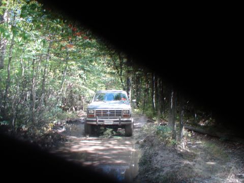 1992 Ford Bronco - This 1992 Ford Bronco navigates a challenging muddy trail surrounded by dense forest.