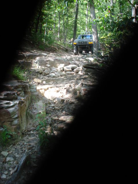 1992 Ford Bronco - Ford Bronco navigates a challenging off-road path through a wooded area.