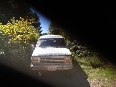 1992 Ford Bronco - A white Ford Econoline van is seen from the front on a dirt road surrounded by trees.