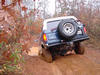 1986 Ford Bronco - An SUV navigates a challenging muddy trail, its rear tire visible as it climbs.