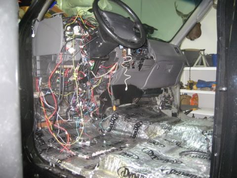 2007 Ford Mustang - The vehicle's interior is disassembled, revealing a complex wiring system and soundproofing material on the floor.