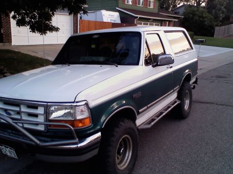 1996 Ford Bronco - This two-tone Ford Bronco features a brush guard and side steps, parked in a residential driveway.