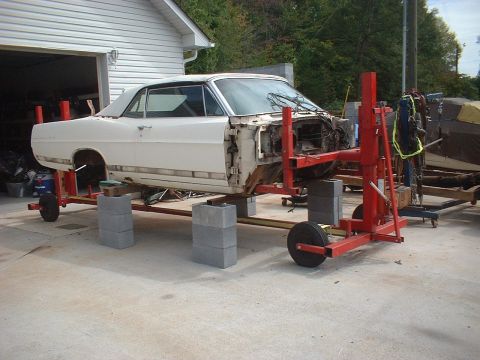 1967 Ford Galaxie - A 1967 Ford Galaxie body is supported by a red frame and wheels, undergoing repairs with its front end disassembled.