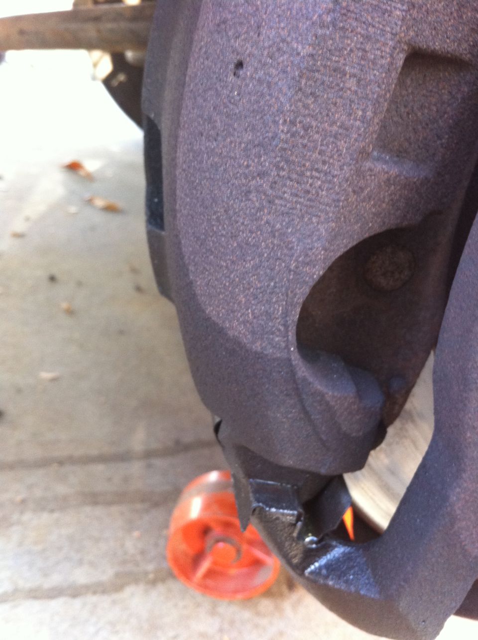 Close-up of a rusty brake caliper with an orange wheel chock nearby