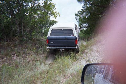 1986 Ford Bronco - Ford Bronco navigates a rough, wooded trail. The vehicle has a two-tone paint scheme.