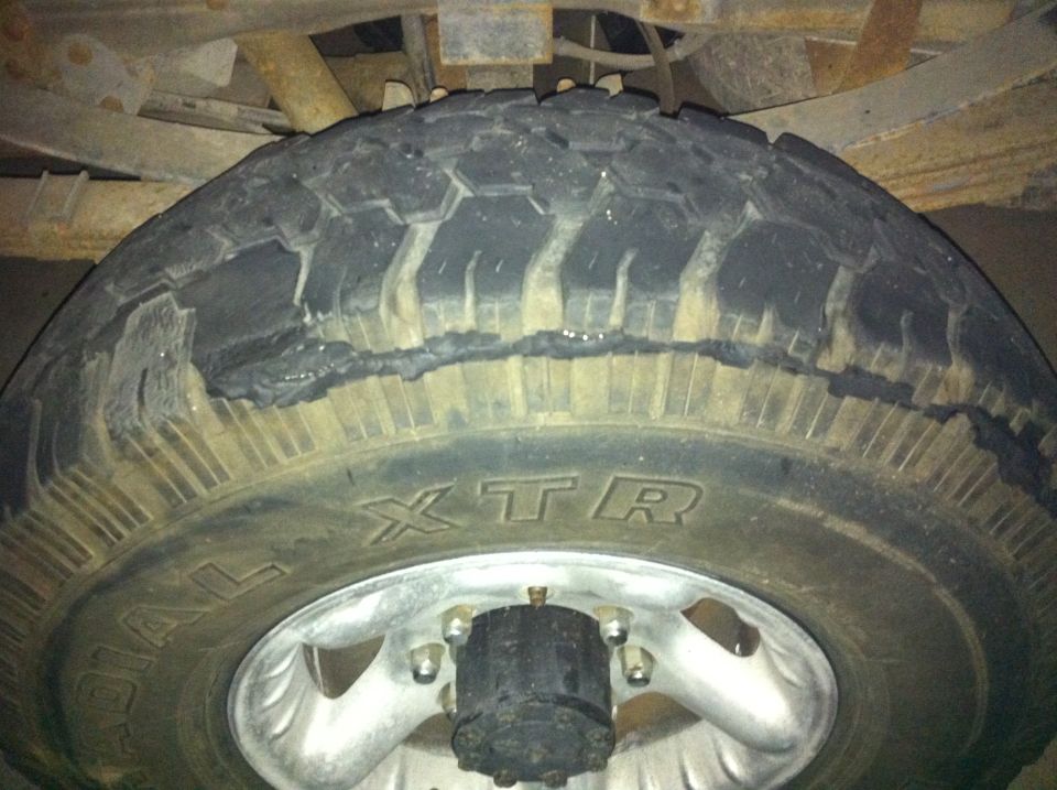 Close-up of a damaged tire with visible tread separation and a Supermotors.net watermark