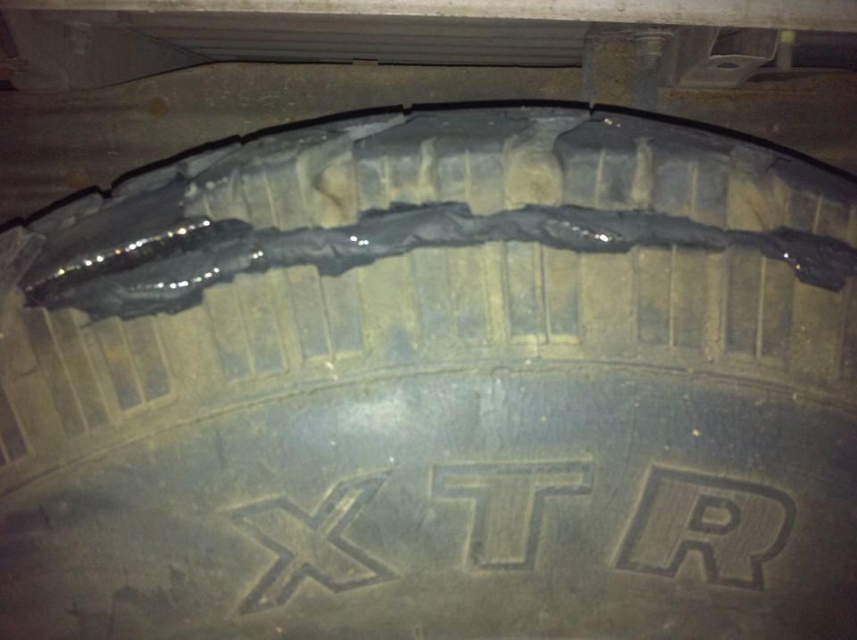 Close-up of a tire with a large section of tread missing and what looks like black sealant applied