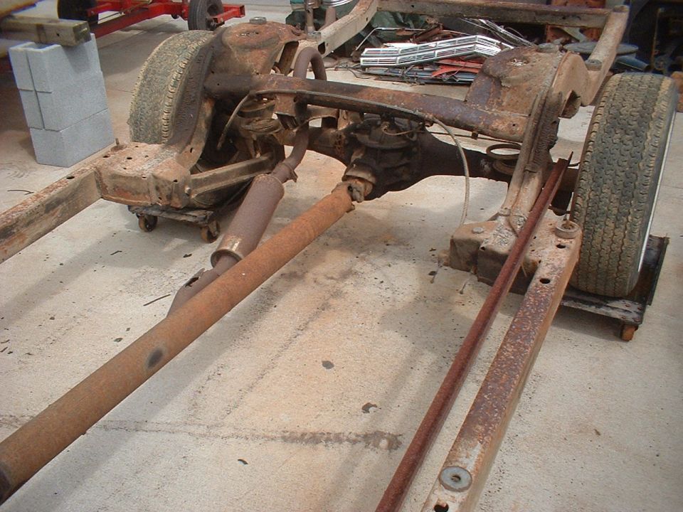 Rusted vehicle frame with rear axle, driveshaft, and exhaust pipe, on casters