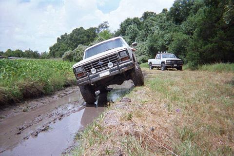 1986 Ford Bronco - A white Ford Bronco navigates a muddy track with another truck in the background.