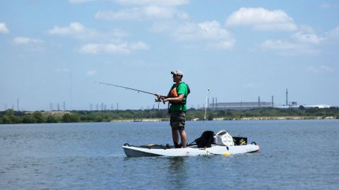 1953 Ford Mainline - Man fishing from a kayak on a lake, with industrial structures visible on the distant shore.