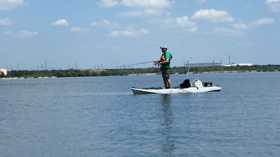 Man standing and casting from a white fishing kayak on calm open water