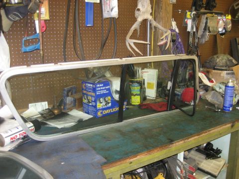 1978 Ford Bronco - Workbench cluttered with automotive parts and tools, a car window assembly.