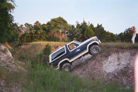 1986 Ford Bronco - A Ford Bronco navigates a challenging off-road terrain, with one wheel lifted off the ground.