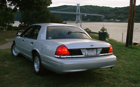 2000 Ford Crown Victoria - A silver 2000 Ford Crown Victoria is parked by the water with a bridge visible in the distance.