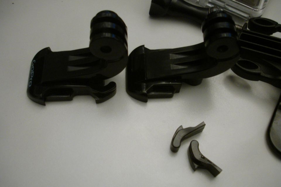 Two black GoPro mounts and some small detached parts are on a white surface. Text 'GoPro' is visible on one mount