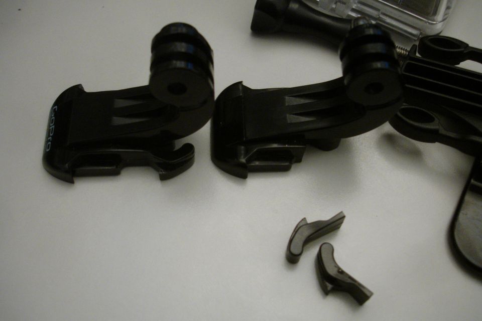Two black GoPro mounts and two small detached plastic pieces on a white surface
