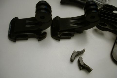 1993 Ford Taurus - Several black GoPro camera mounts and two small, broken plastic pieces are scattered on a white surface.