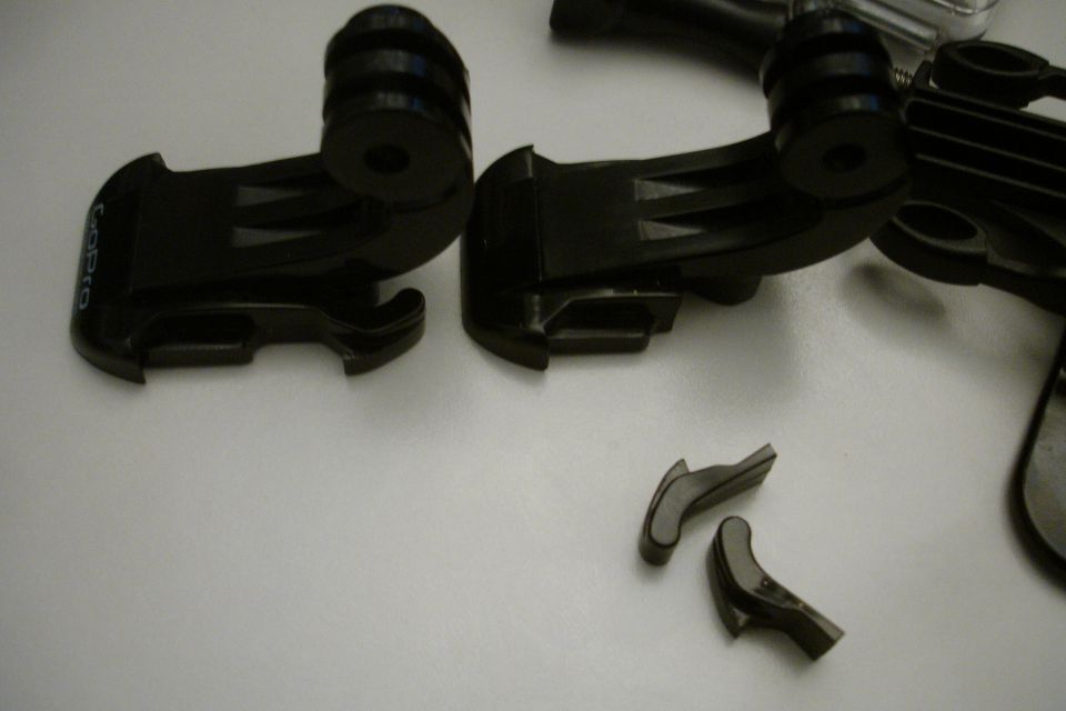 Black GoPro mounts and small broken plastic pieces on a white surface