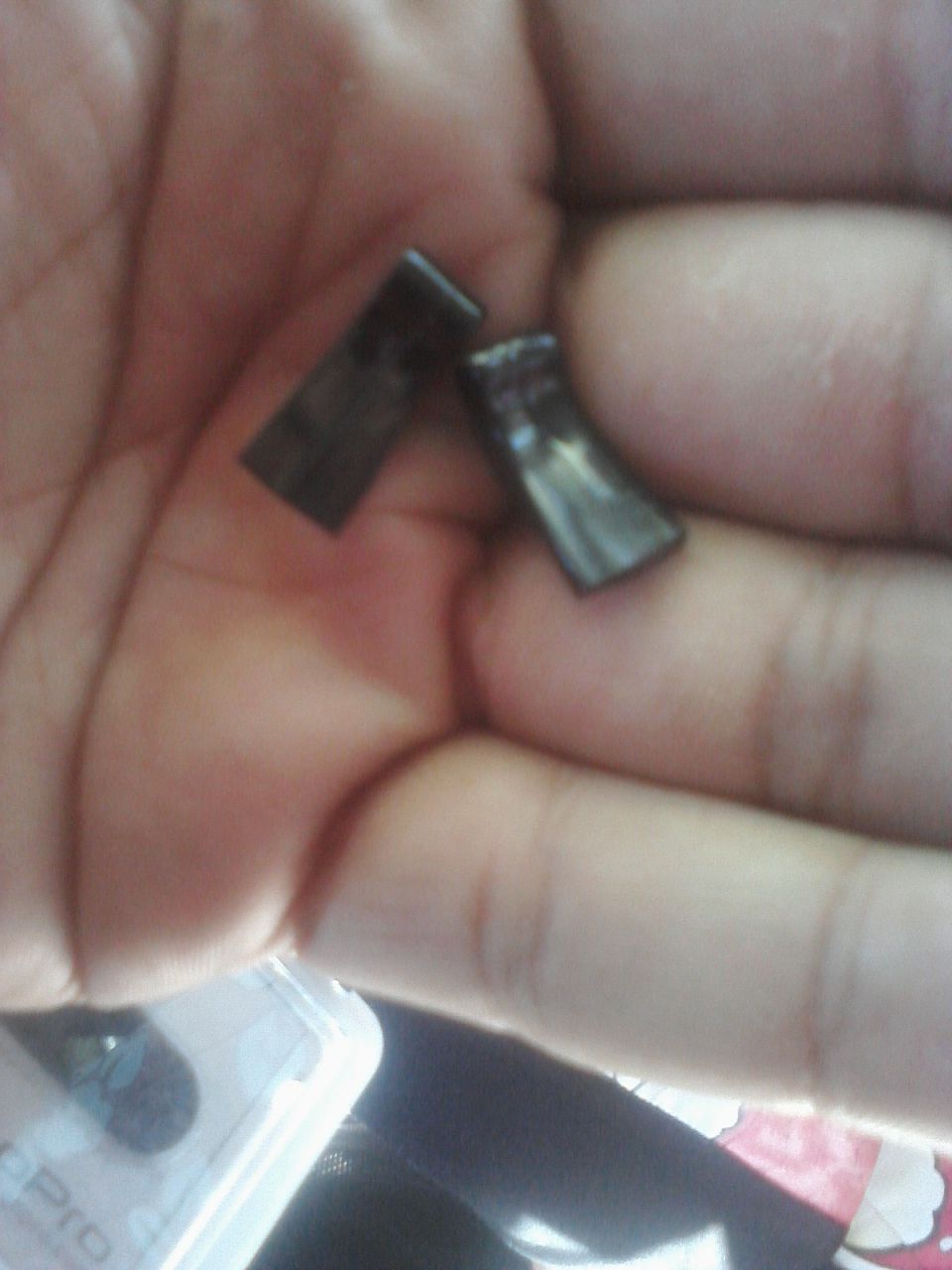 two small, dark, rectangular metal pieces held in a palm