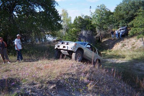 1986 Ford Bronco - Off-road vehicles navigate a challenging dirt trail surrounded by trees and vegetation.