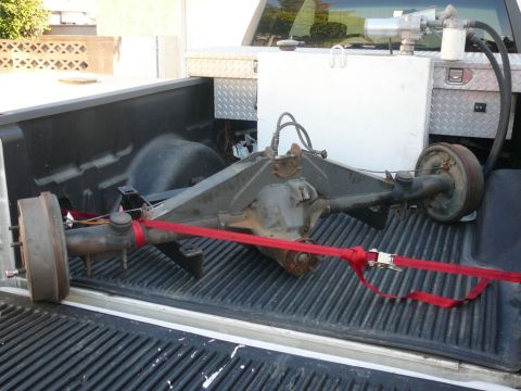 1988 Ford Bronco - A rear axle assembly is transported in the bed of a pickup truck, secured with red tie-down straps.