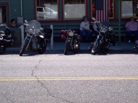 1999 Ford Crown Victoria - Several motorcycles are parked in a row along the curb in front of a building displaying an American flag.