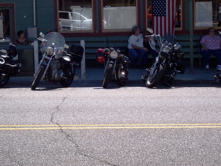 Three motorcycles parked on a street in front of a building with an American flag