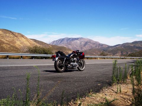 1999 Ford Crown Victoria - Motorcycle parked on a scenic roadside with mountains under a clear blue sky.