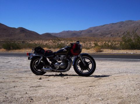 1999 Ford Crown Victoria - A motorcycle is parked on the side of a desert road under a clear blue sky.