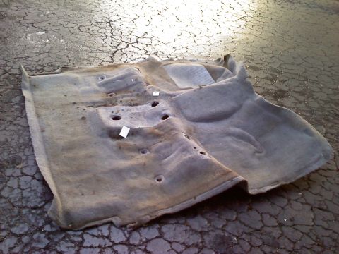 1995 Ford Bronco - Removed vehicle carpet lying on cracked pavement.
