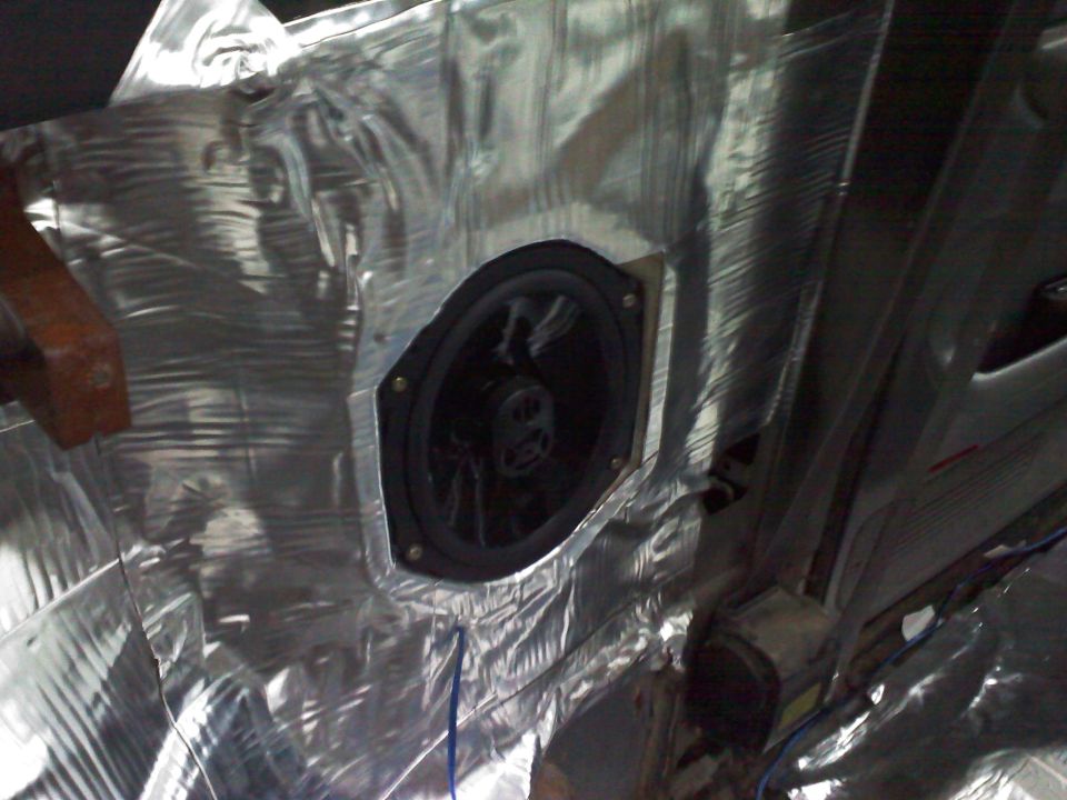 Car door panel covered in silver sound deadening material with a speaker installed