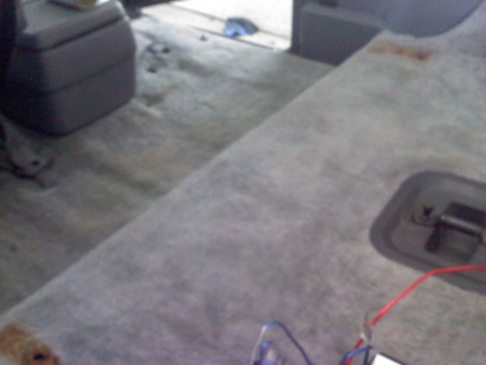 Interior shot of a vehicle's carpeted floor and rear seat area, showing a center console and some wiring