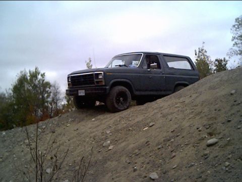 1981 Ford Bronco - A dark gray Ford Bronco is parked on a dirt incline under an overcast sky.