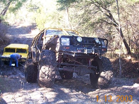 1986 Ford Bronco - Two off-road vehicles are stuck in the mud on a wooded trail.