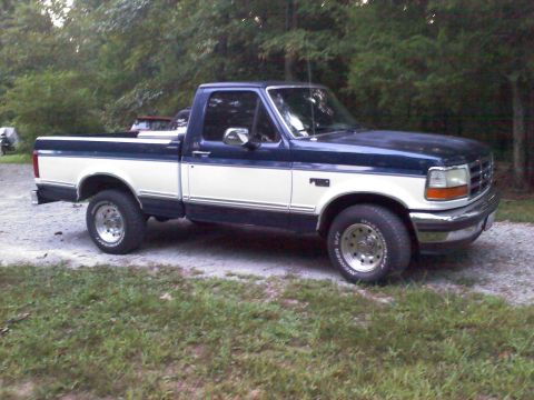 1995 Ford F-150 - This two-tone blue and white 1995 Ford F-150 pickup truck is parked on a gravel surface.
