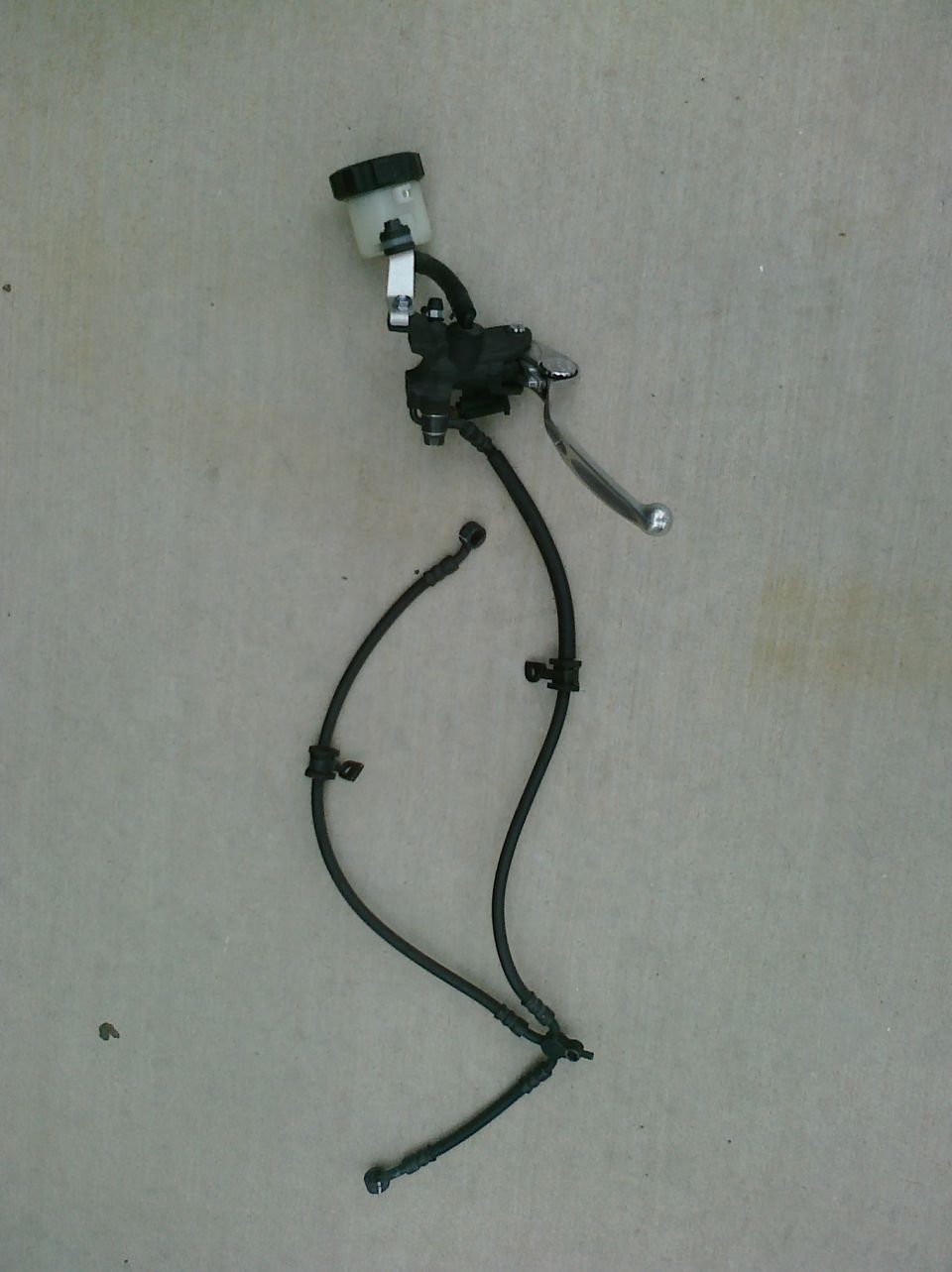 Motorcycle brake master cylinder with reservoir and lines laid out on a flat surface