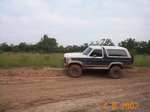 1986 Ford Bronco - A classic Ford Bronco sits off-road on a dirt path under an overcast sky.