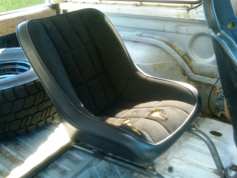 1986 Ford Bronco - The interior of a vehicle shows a worn bucket seat and a spare tire, with visible rust on the interior panels.