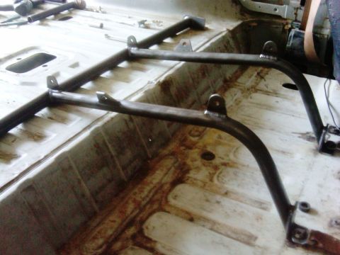 1986 Ford Bronco - A custom roll cage is being installed inside a vehicle's interior, with visible metalwork and floor mounts.