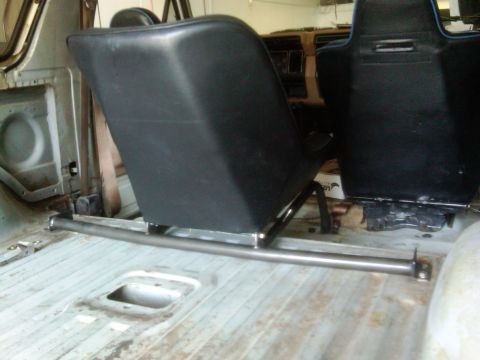 1986 Ford Bronco - Aftermarket bucket seats are installed in the interior of a vehicle, with a metal support bar visible on the floor.