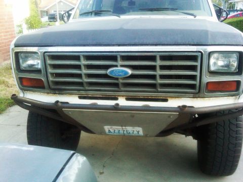 1986 Ford Bronco - The front grille and bumper of a 1986 Ford Bronco are visible, a Ford logo and an aftermarket bumper with a license plate.