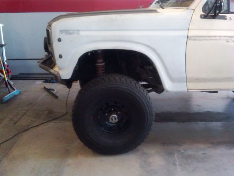 1986 Ford Bronco - Close-up of a truck's front wheel well and fender, showing suspension components and a large tire.